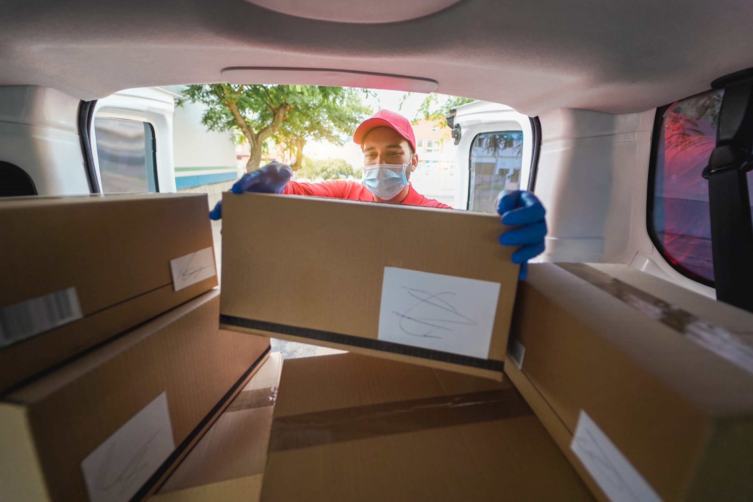 Courier man with safety mask holding cardboard box for delivery - Focus on face